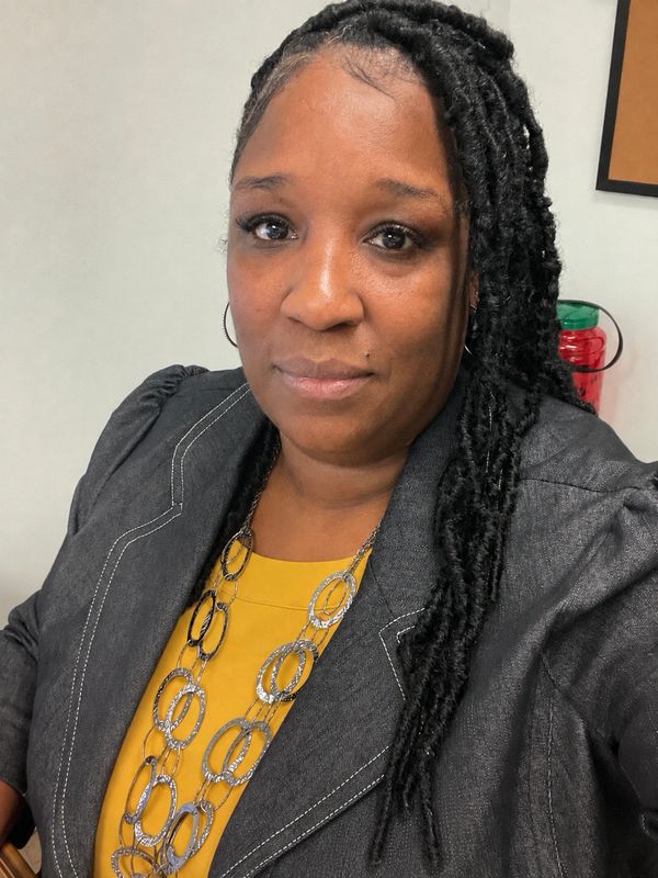 Woman with braided hair wearing a gray blazer and yellow top.