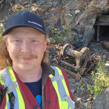 Man in safety vest takes selfie near old machinery and cave.