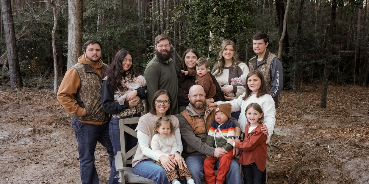A large family posing outdoors in a wooded area during fall.