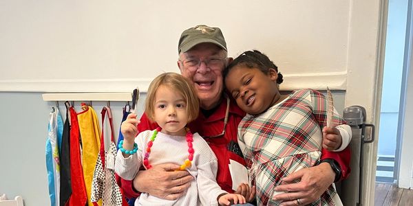An elderly man joyfully hugs two young children, one holding feathers.