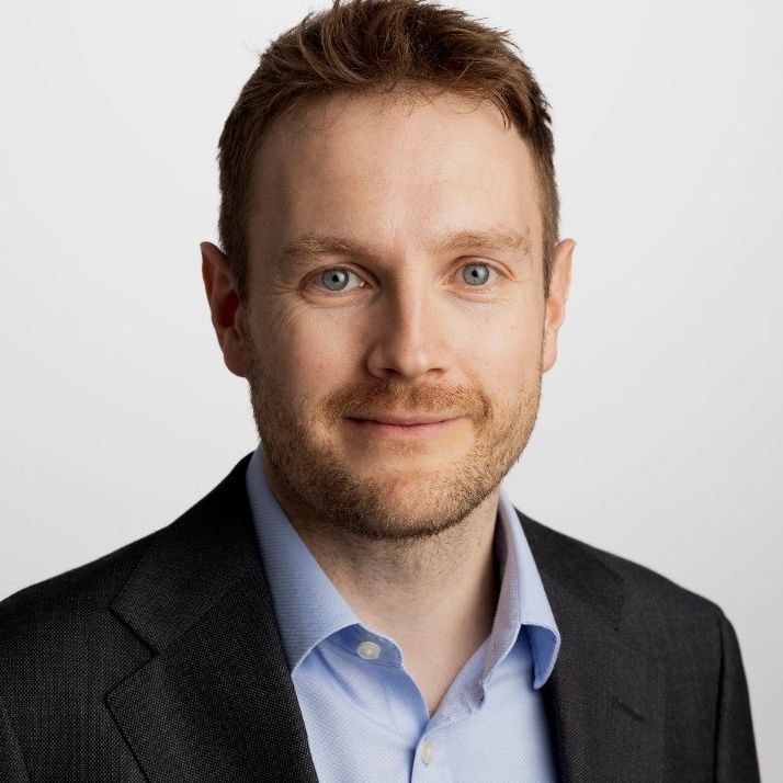 Man with light brown hair wearing suit jacket and blue shirt.