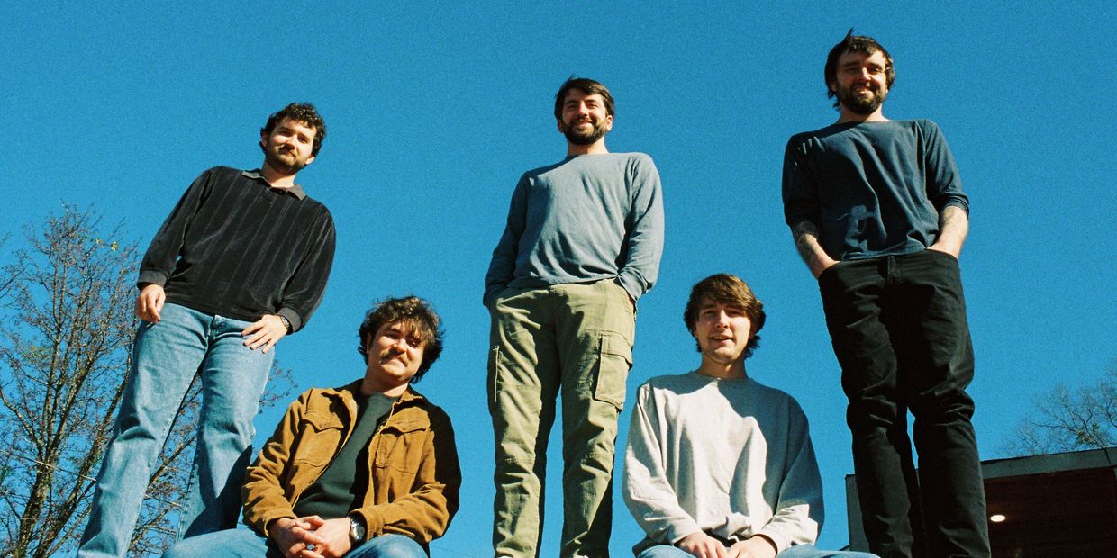 Five young men posing outdoors against a clear blue sky.