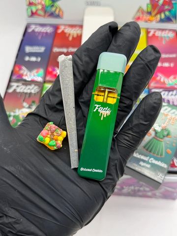 Hand holds a green Fade vape, a joint, and a colorful edible treat.