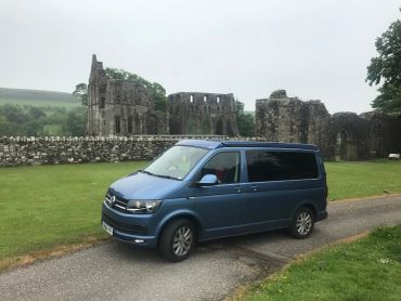 Blue Volkswagen van parked near ancient stone ruins.
