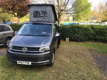 Volkswagen campervan with pop-up roof in a park.
