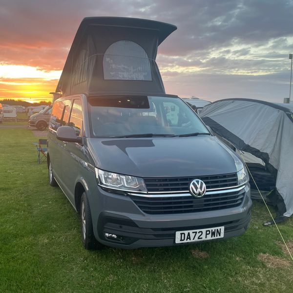 Volkswagen campervan with pop-up roof at sunset.