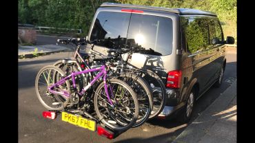 Three bicycles mounted on the rear of a black van.