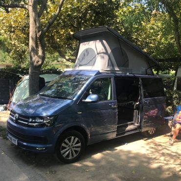 Blue camper van with raised roof in a campground.