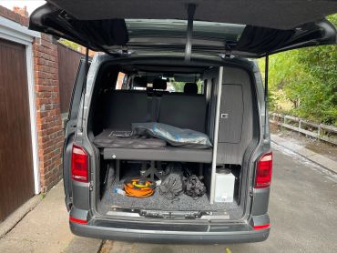 Open back of a gray camper van showing storage and bedding.