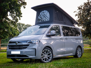 Silver camper van with a raised roof tent parked on grass.