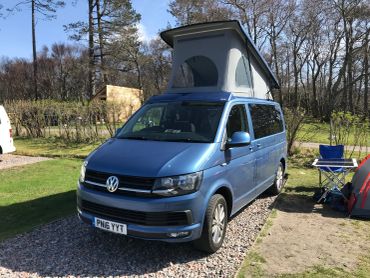 Blue Volkswagen camper van with a pop-up roof in a campsite.