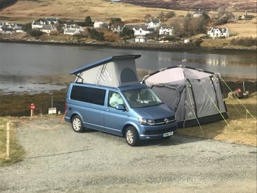 Blue camper van with pop-up roof next to a tent by the water.