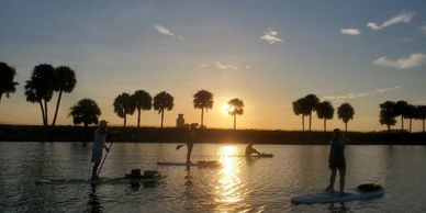 People paddleboarding on a lake during sunset.