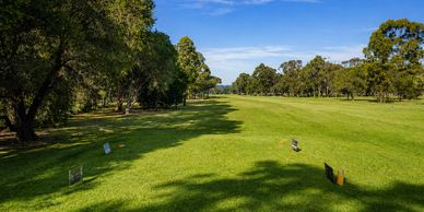 A sunny golf course fairway lined with trees under a clear blue sky.
