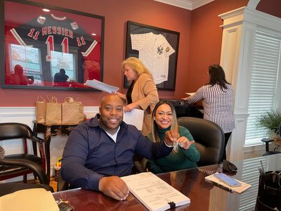 Happy couple signs papers indoors with two women working in the background.