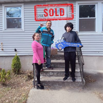 Familia posando frente a su casa recién vendida con letrero de vendido.