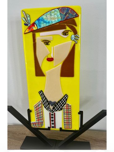 Colorful cubist-style glass art of a woman with a hat on a yellow background.