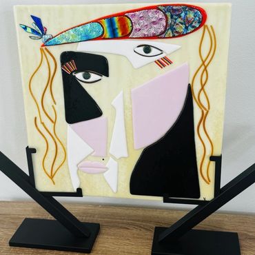 Abstract colorful glass artwork depicting a stylized face on a stand.