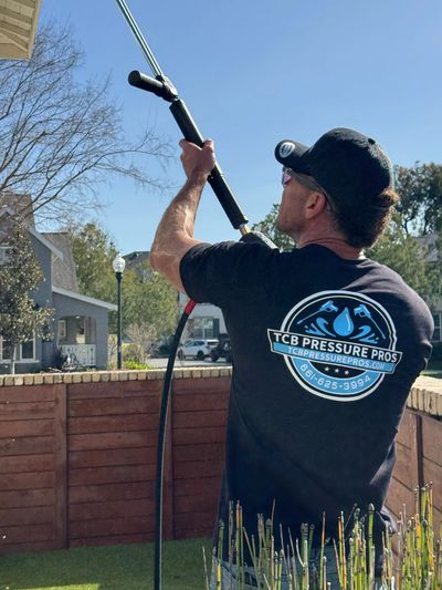 Man in TCB Pressure Pros shirt using a pressure washer outdoors.
