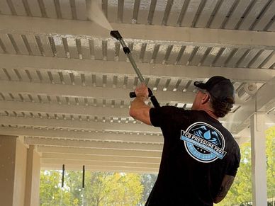 Man pressure washing a pergola ceiling outdoors.
