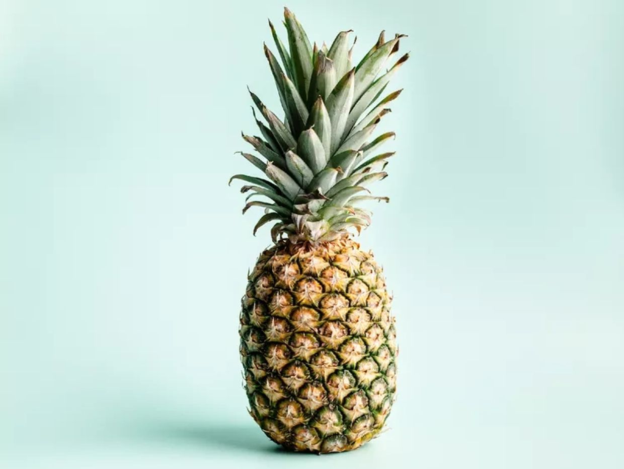 A ripe pineapple with green leaves on a light blue background.