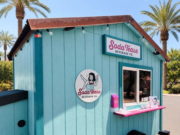 Small teal beverage stand with pink accents under palm trees.