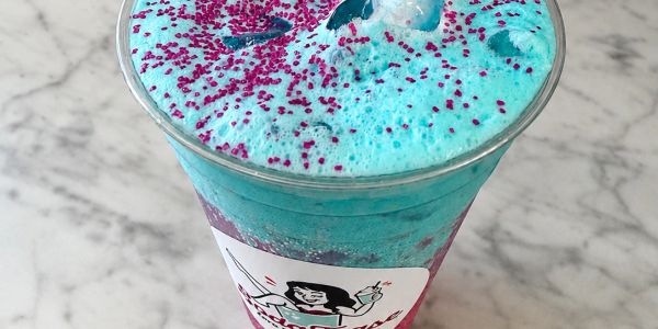 Blue fizzy drink with purple sprinkles in a plastic cup.