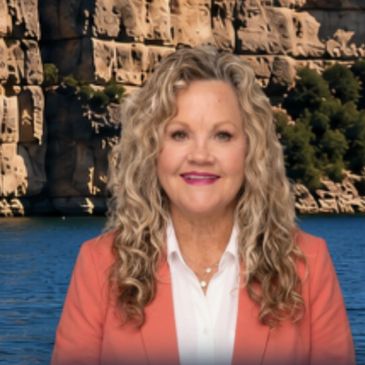 Woman with curly blonde hair in coral jacket by water.