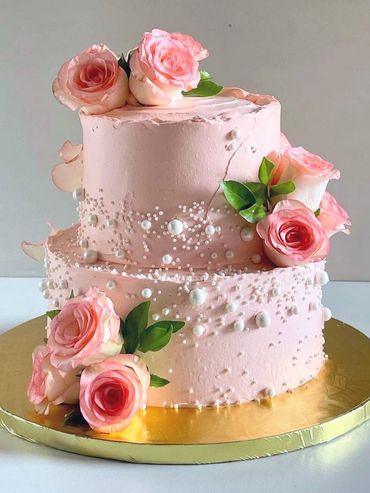 Elegant two-tier pink cake adorned with fresh roses and pearl decorations.
