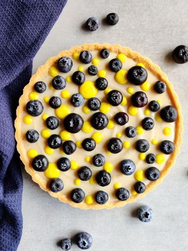 Blueberry tart with yellow custard dots on a light surface.
