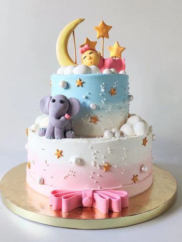 Two-tier pastel cake with moon, stars, sleeping baby, and elephant decorations.