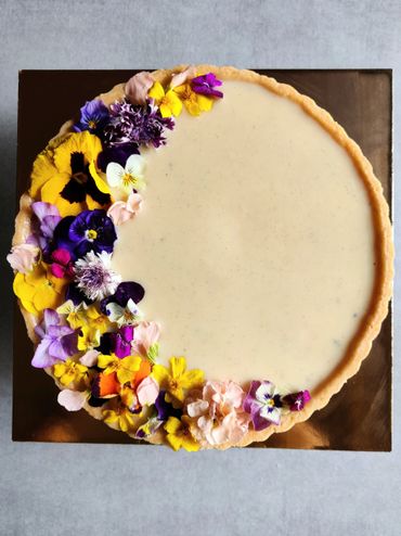 A creamy tart decorated with colorful edible flowers on one side.
