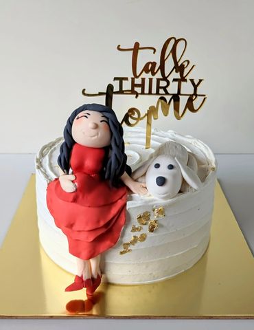 White cake with figurines of a woman in a red dress and a dog, topped with 'tall thirty one' text.