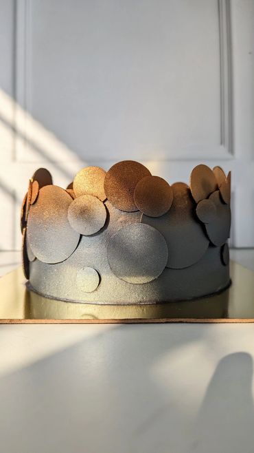 A modern cake decorated with metallic circular discs in golden and bronze hues.