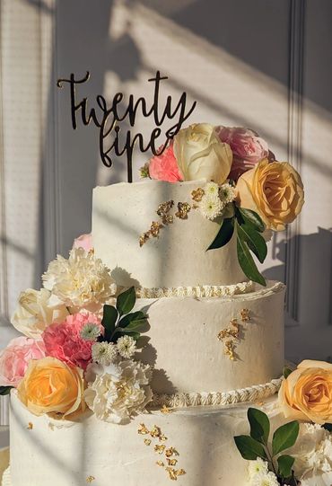 Elegant three-tier cake decorated with fresh flowers and "Twenty five" topper.