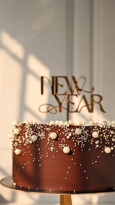 Chocolate cake with pearl decorations and a 'New Year' topper.
