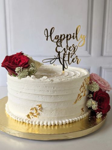 Elegant white cake with red roses and gold 'Happily Ever After' topper.
