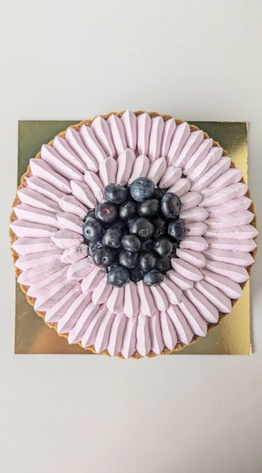 Round tart with purple cream and fresh blueberries on top.