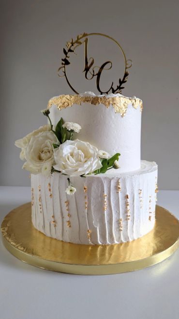 Elegant two-tier white cake with gold accents and white flowers.