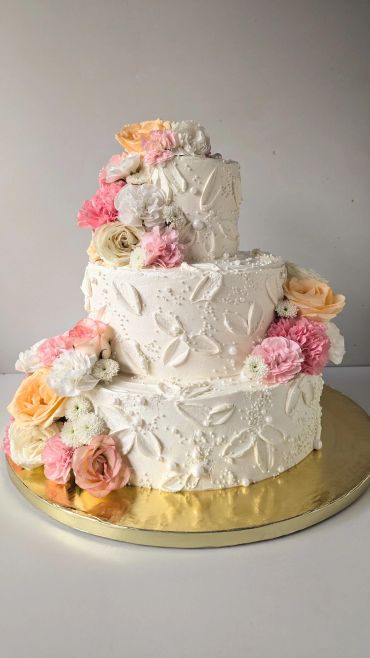 Elegant three-tier white cake decorated with pastel flowers and intricate icing patterns.