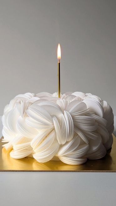 Elegant white cake with intricate petal-like frosting and a single gold candle.