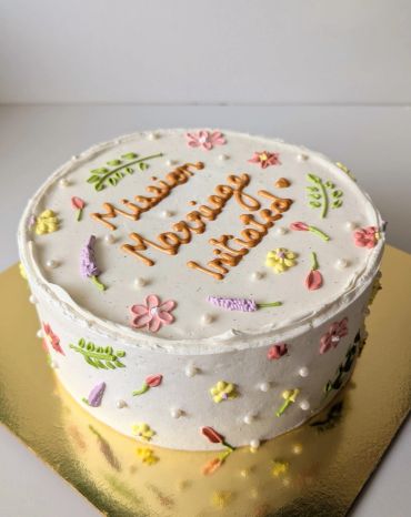 White cake with floral decorations and orange writing.