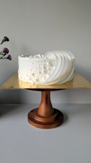 Elegant white cake with pearl decorations on a wooden stand.