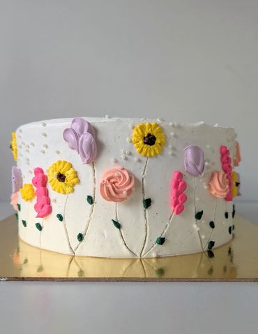 White cake decorated with colorful buttercream flowers and leaves.