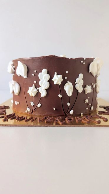Chocolate cake with white floral decorations on a gold board.
