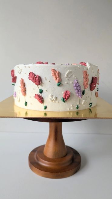 Elegant white cake decorated with colorful floral icing on a wooden stand.