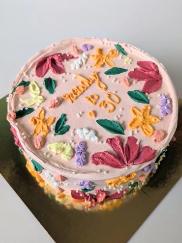 A round pink cake decorated with colorful buttercream flowers and the text "ready to 30".