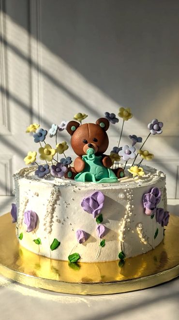 Decorative cake featuring a bear and pastel flowers.