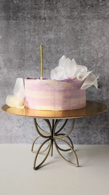 Elegant pastel purple cake with white floral decorations on a gold stand.
