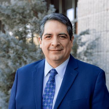 Professional man in a blue suit smiling outdoors near a building.